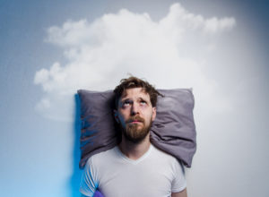 Man having problems/ insomnia, laying in bed on pillow, looking up to gray cloud over his head, copy space